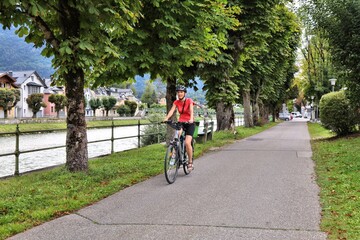Naklejka premium Tourist on a bicycle along River Traun in Bad Ischl, Salzburg State, Austria. Woman cyclist on Salzkammergut Cycling Route (Salzkammergut-Radweg).