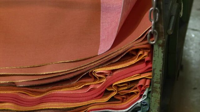 Large stacks of orange textile fabrics stored inside a textile factory. Materials are organized and prepared for further processing in garment manufacturing.