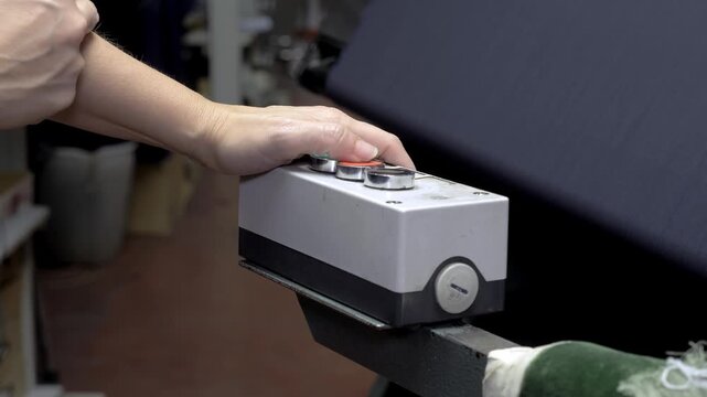 Close-up of a factory worker hand pressing control buttons on an industrial textile machine. The operator manages production equipment inside a textile manufacturing facility.