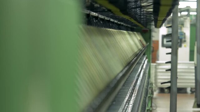 Industrial textile equipment processes raw wool fibers during manufacturing. The production machine transforms the material into textile products inside a factory environment.