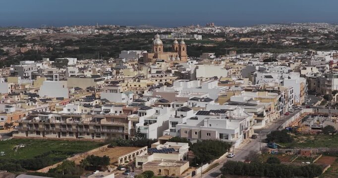 Aerial view of the Dingli Parish Church surrounded by a cluster of buildings and lush greenery, creating a beautiful contrast, Dingli, Malta.