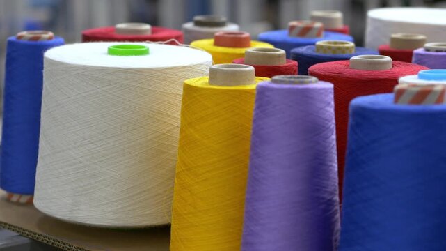 Multicolored wool rolls arranged in stacks inside a textile factory. The prepared fibers will be used for future fabric manufacturing and garment production.