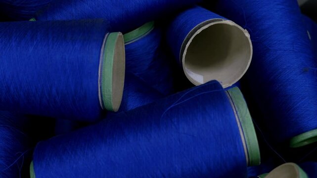 Rolls of colored wool fibers stacked inside a textile factory. The material is prepared for fabric manufacturing and clothing production processes.