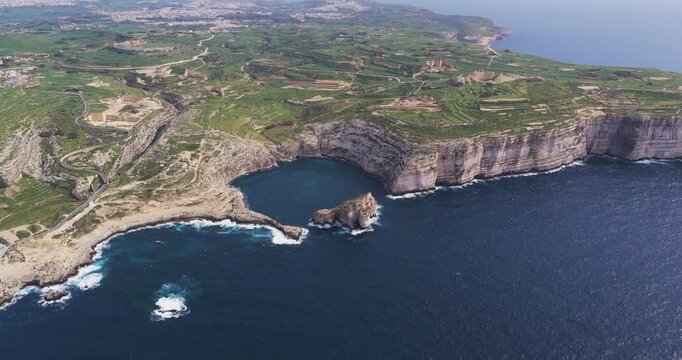 Aerial view of the rugged Dwejra Bay coastline where the turquoise sea meets the tall, light-colored cliffs along the green landscape, Dwejra Bay, Gozo Island, Malta.