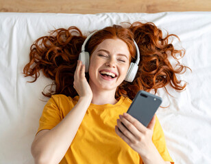 Lachendes rothaariges Mädchen liegt auf dem Bett und hört Musik