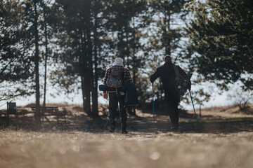 Obraz premium Two hikers walk away from the camera on a forest path with backpacks and trekking poles. The scene captures outdoor adventure and companionship in a quiet, natural setting.