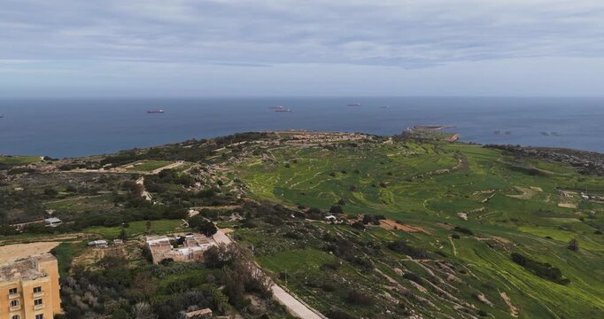 Aerial view of the Mellieha coastline with ships sailing on the horizon, a blend of green fields and rocky terrain, Mellieha, Mellieha, Malta.
