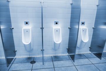 Row of white urinals with stainless steel partitions in a clean public male restroom