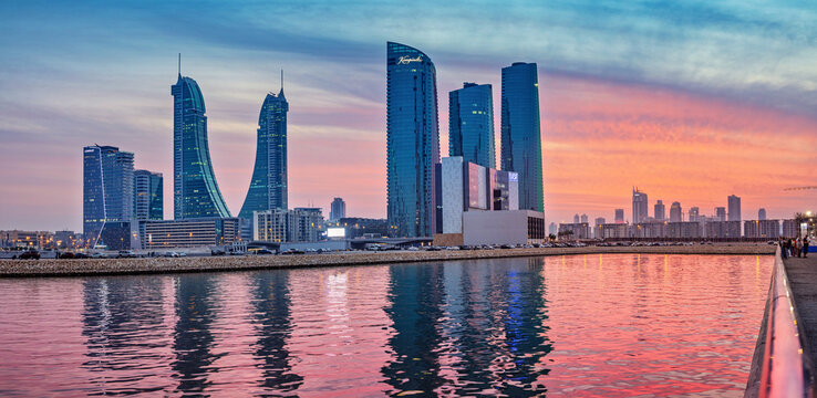 2 December 2025, Bahrain, Manama: skyline buildings reflecting vibrant sunset colors on the calm bay water
