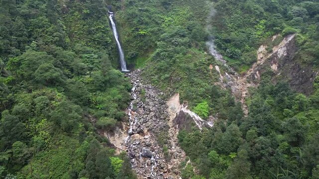Natural beauty of Curug Cikawah waterfall lies adjacent to a volcanic crater, surrounded by dense rainforest and rugged terrain in Bogor, Indonesia. Ideal for promoting tourism, and nature projects.