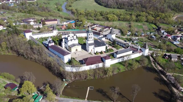 Breathtaking drone shot of Paphnutiev Borovsk Monastery, a beautiful spiritual landmark with white walls and domes, surrounded by tranquil Russian nature. Borovsk, Kaluga region, Russia