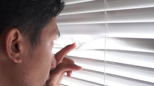 Curious man looking through venetian blind