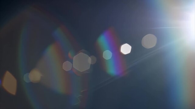 Soft focus abstract of a diagonal rainbow arc with hexagonal light flares against a dark background