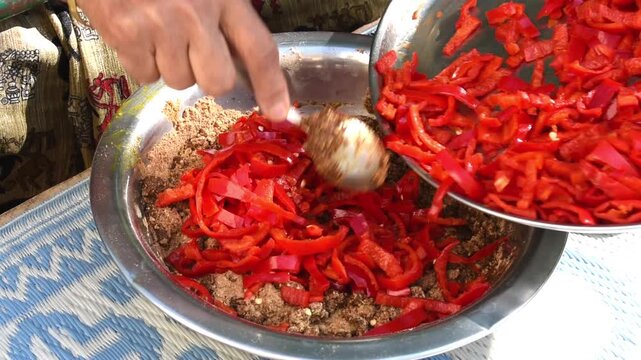 putting cut red chilli or pepper to powdered masala for making traditional pickle or achar, mota lal mirch ka achar.