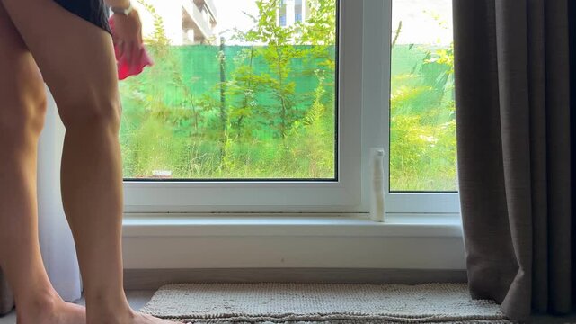 Cleaning floor to ceiling windows with cloth in home interior. Window washing routine and bright organized living space concept.