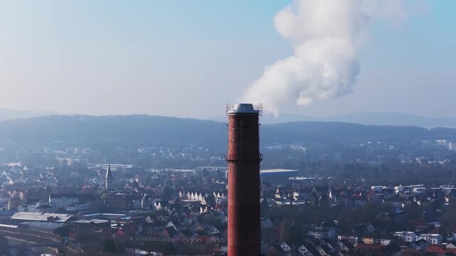 Aerial perspective of industrial smokestack emitting steam over city of Bielefeld in Germany, icon of industrial energy production