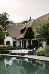 Obraz premium Modern house with a thatched roof located near a pool surrounded by green plants during a cloudy day in a residential area