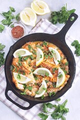 Delicious haddock fish piccata with lemon and capers in cast iron pan, vertical, top view