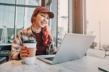 Smiling woman working on laptop, enjoying coffee in a modern cafe. Exploring remote work and freelance lifestyle