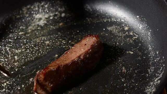 Chef basting beef steak with melted butter in cast iron skillet during searing, slow motion close-up of liquid cascading over meat surface with rising vapor