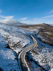 Aerial view of a winding mountain road surrounded by snow under a blue sky