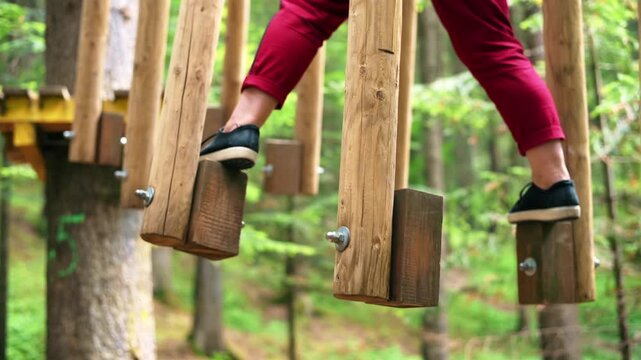 Woman crossing unstable wooden bridge on ropes course in forest adventure park during summer vacation