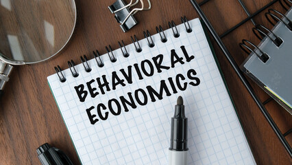 BEHAVIORAL ECONOMICS top view of an open notebook with text. magnifying on notepad page on wooden...