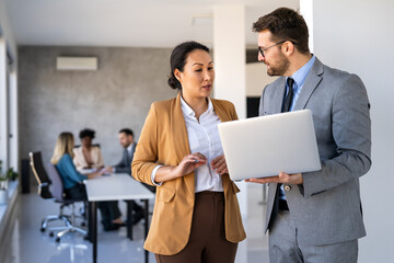 Two happy diverse multiethnic business team people working, talking in corporate office