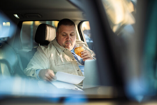 Man eating pastry and reviewing paperwork in car