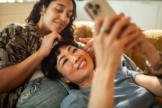 Two women relaxing on couch at home using smartphone