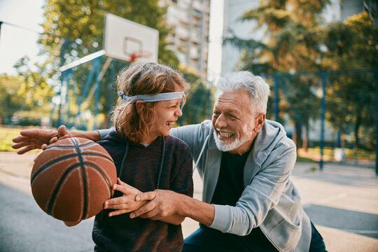 Grandfather coaching grandson playing basketball at city park