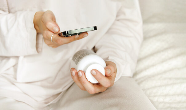 Woman using her mobile phone to search details about her pills medication. Research reading information about vitamins supplements online, side effects or benefits, health care application.	