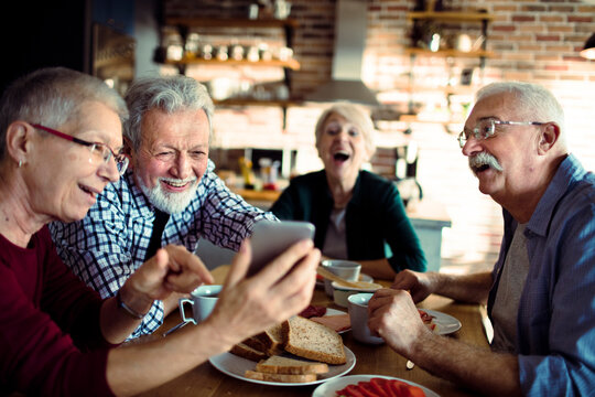 Senior friends laughing over smartphone at kitchen table