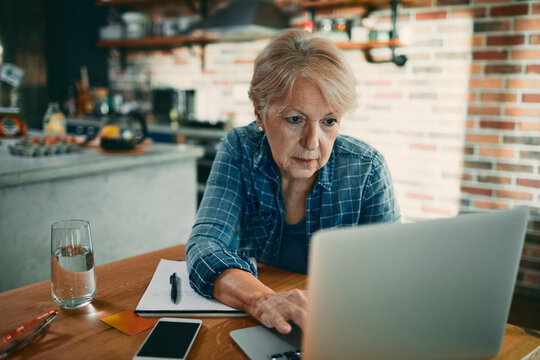 Senior woman working on laptop at home kitchen table