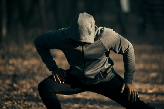 Hooded athlete warming up with side lunge in forest park