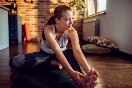 Focused young woman stretching on yoga mat at home