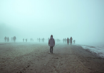 People walking in thick fog along a sandy shore