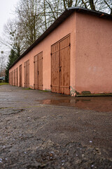 Fototapeta premium Empty Road Beside Old Garages in Quiet Residential Area. Simple architecture, wet pavement, and neutral tones emphasize everyday urban infrastructure and calm city life without people.