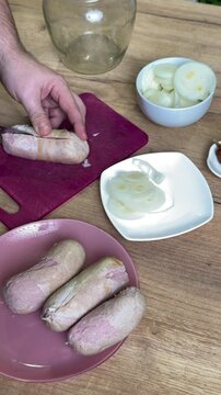 Man slicing a sausage lengthwise. Stuffing it with onion rings. For making pickled sausages. Vertical video.
