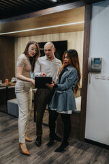 Three colleagues review information on a tablet in a contemporary workspace. They collaborate closely, sharing ideas in a professional office setting.