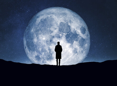 Human stands silhouetted against a luminous full moon