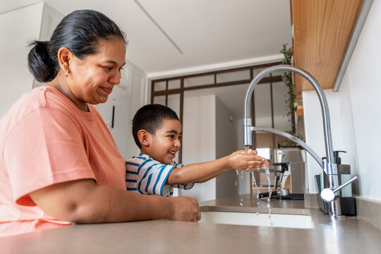 Mother helping son wash hands at kitchen sink