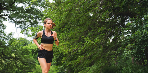 Active young woman jogging in public park on summer morning