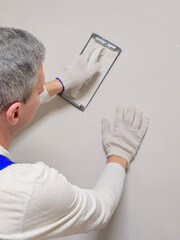 Vertical view the hand of a worker and a tool for grinding putty.