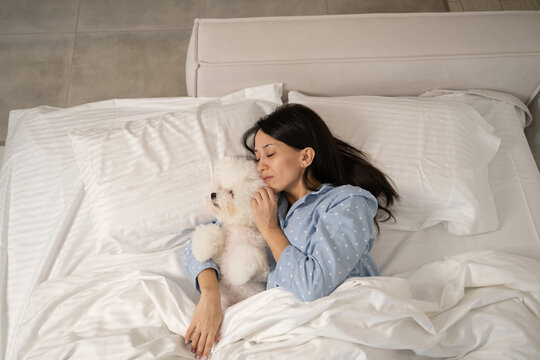Woman in bed snuggling with a fluffy white dog