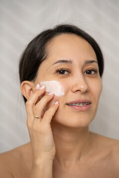 Woman applying face cream at home