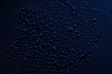 Water droplets form patterns on a dark surface in the evening light creating a unique visual effect in a close-up view