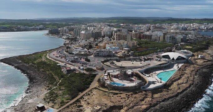 Aerial view of buildings and pools contrasting with the rocky coastline and city buildings, St. Paul's Bay, Malta.