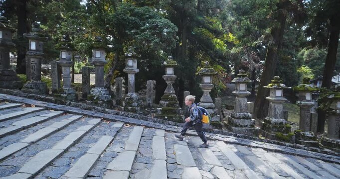 Happy little boy walking alone up steps near ancient, worn lanterns in Japanese village