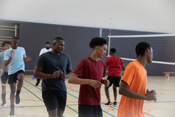 African American adolescent males in shorts running drills through orange rings, ladders in gym